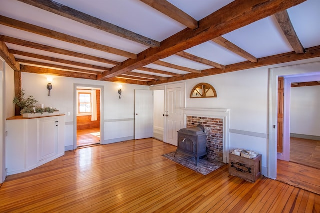 unfurnished living room with beam ceiling, a wood stove, baseboards, and light wood finished floors