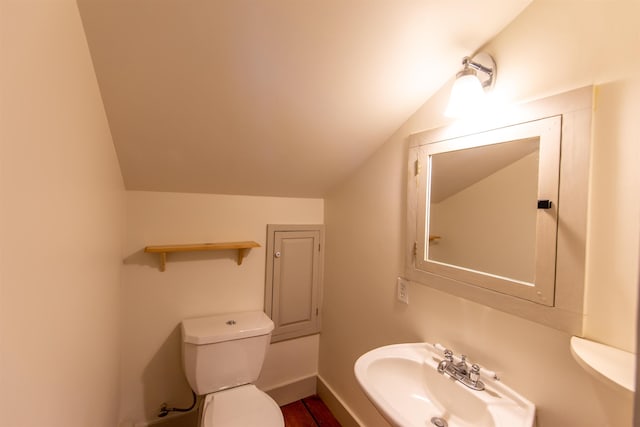 half bathroom featuring vaulted ceiling, toilet, baseboards, and a sink