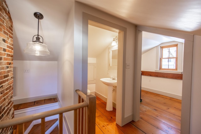 corridor with baseboards, lofted ceiling, a sink, light wood-style floors, and an upstairs landing