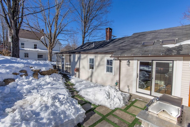 snow covered house with a chimney and roof with shingles