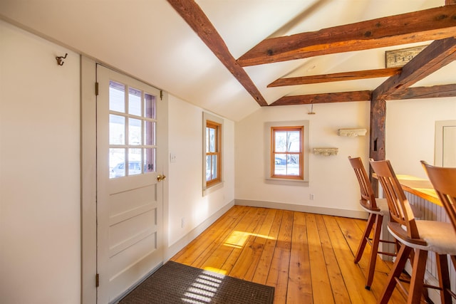 interior space with light wood-style flooring, vaulted ceiling with beams, and baseboards