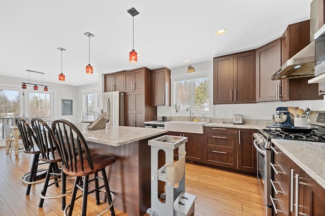 kitchen featuring light wood finished floors, a kitchen breakfast bar, appliances with stainless steel finishes, wall chimney range hood, and a center island