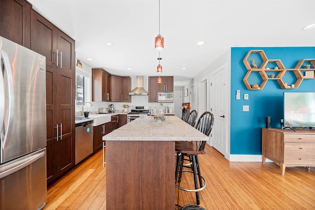 kitchen featuring a kitchen island, wall chimney range hood, a breakfast bar, light wood-type flooring, and appliances with stainless steel finishes