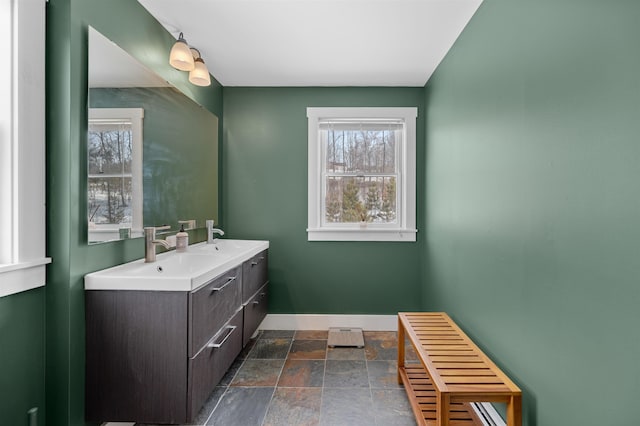 bathroom with double vanity, baseboards, stone tile flooring, and a sink