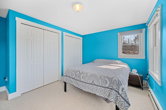 carpeted bedroom featuring a baseboard heating unit, baseboards, and two closets