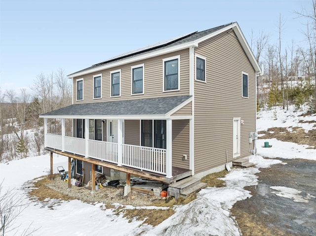 view of front of house with solar panels, a porch, and roof with shingles