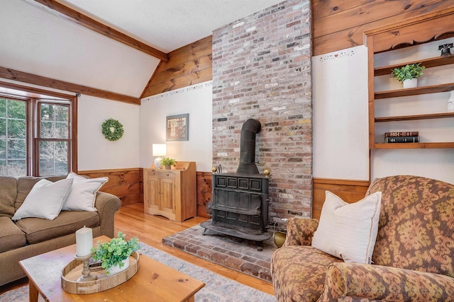 living area featuring wood walls, lofted ceiling with beams, light wood-style flooring, wainscoting, and a wood stove