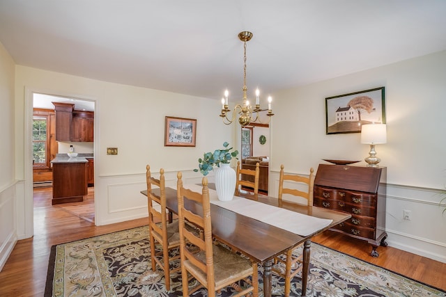 dining space featuring a wainscoted wall, light wood-type flooring, a baseboard heating unit, and a chandelier