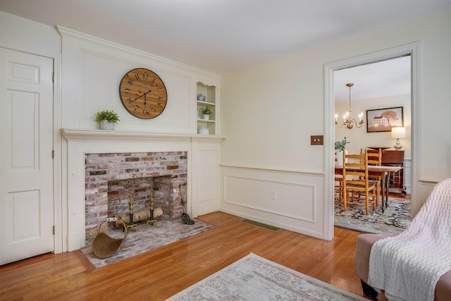 living area featuring visible vents, built in shelves, a notable chandelier, a wainscoted wall, and wood finished floors