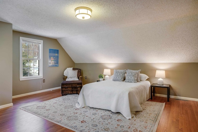 bedroom featuring baseboards, a textured ceiling, wood finished floors, and vaulted ceiling