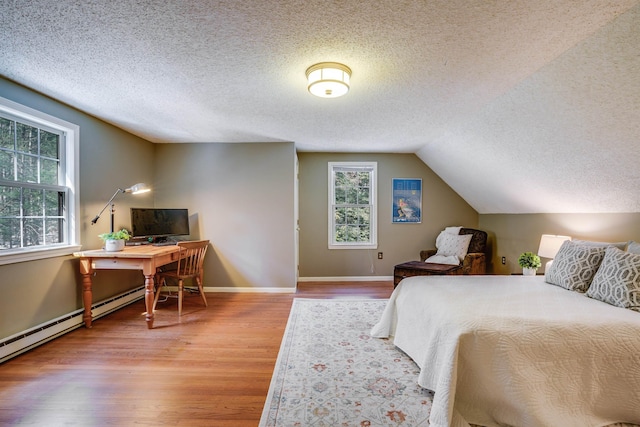 bedroom with lofted ceiling, a baseboard heating unit, a textured ceiling, wood finished floors, and baseboards