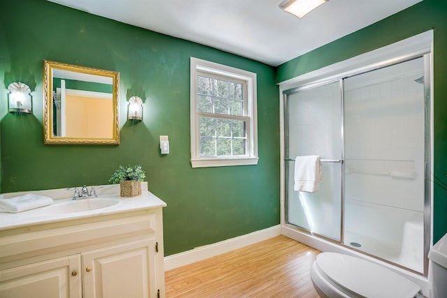 bathroom featuring toilet, wood finished floors, a shower stall, baseboards, and vanity