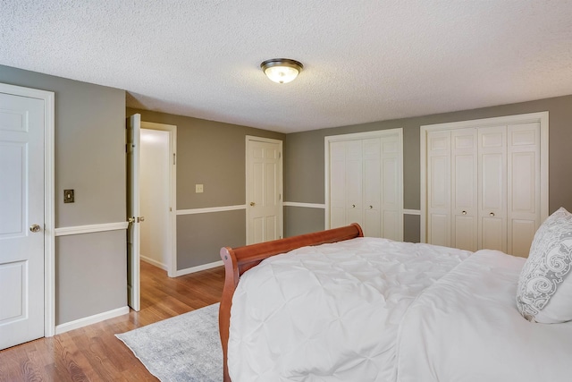 bedroom with baseboards, multiple closets, a textured ceiling, and wood finished floors