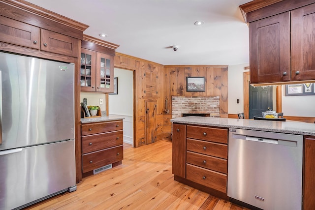 kitchen featuring wooden walls, visible vents, light wood finished floors, stainless steel appliances, and glass insert cabinets