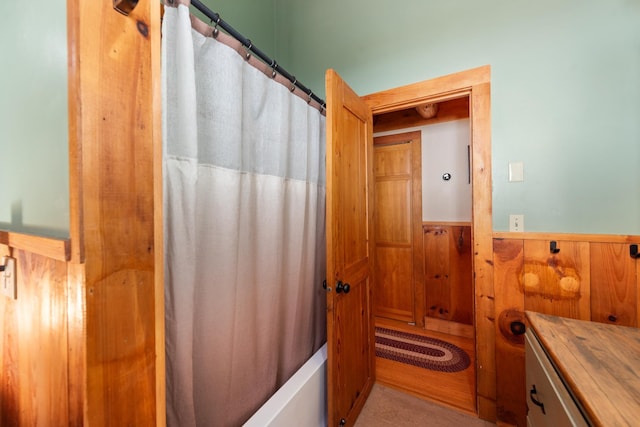 bathroom featuring wooden walls, shower / tub combo with curtain, and wainscoting