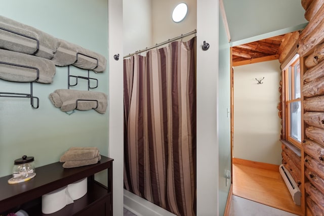 full bath with a shower with curtain, wood finished floors, a baseboard radiator, and rustic walls