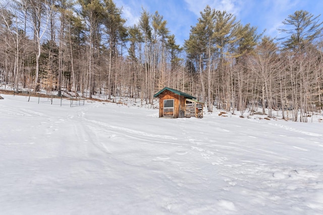 yard layered in snow featuring an outdoor structure and a wooded view