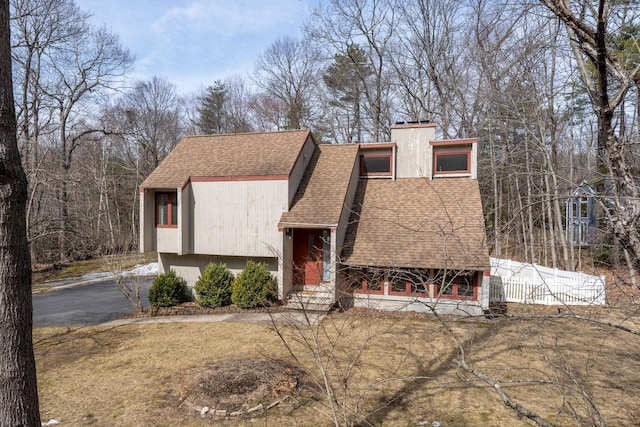 view of front facade with aphalt driveway, a chimney, roof with shingles, and fence