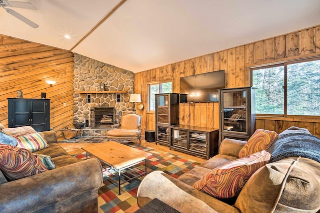 living area with a stone fireplace, lofted ceiling, a ceiling fan, and wood walls