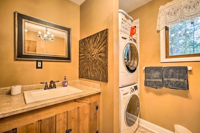 washroom featuring a notable chandelier, stacked washer and dryer, a sink, baseboards, and laundry area