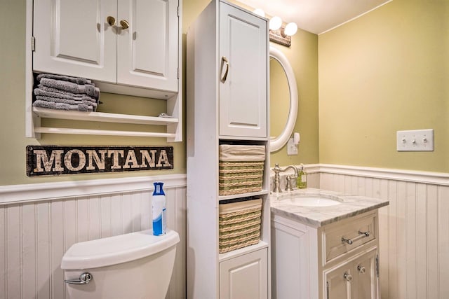 half bath featuring a wainscoted wall, toilet, and vanity