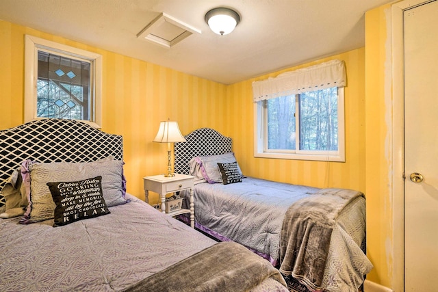 bedroom featuring multiple windows, attic access, and wallpapered walls