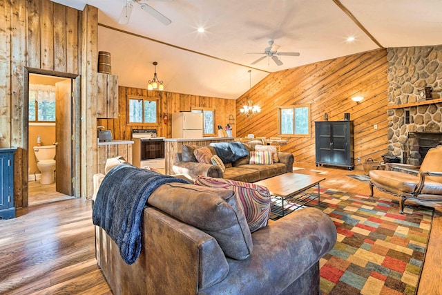 living area with wooden walls, wood finished floors, vaulted ceiling, and ceiling fan with notable chandelier