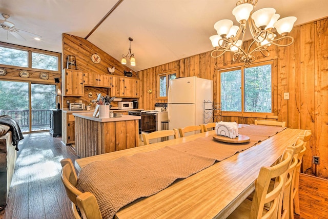 dining area featuring ceiling fan with notable chandelier, wooden walls, dark wood-style floors, and high vaulted ceiling