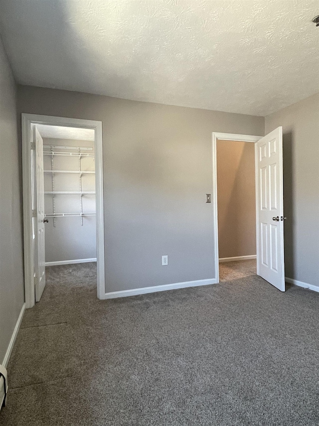 unfurnished bedroom featuring a textured ceiling, a walk in closet, baseboards, and carpet floors