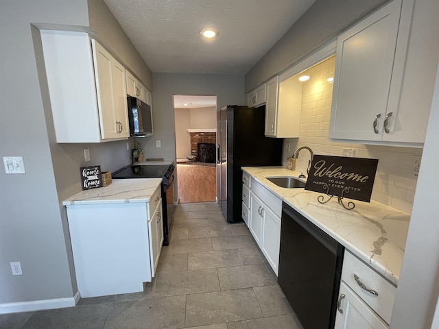 kitchen with black appliances, a sink, white cabinetry, decorative backsplash, and light stone countertops