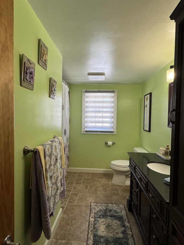 full bathroom with toilet, stone finish floor, curtained shower, baseboards, and vanity