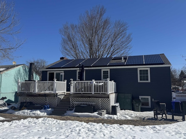 snow covered house featuring roof mounted solar panels and a wooden deck