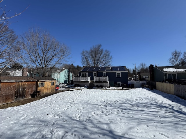 snow covered back of property with roof mounted solar panels and fence