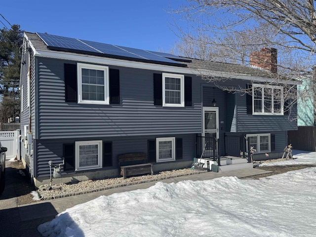 split foyer home with fence, roof mounted solar panels, and a chimney