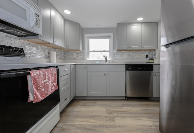 kitchen with light wood finished floors, stainless steel appliances, light countertops, and a sink