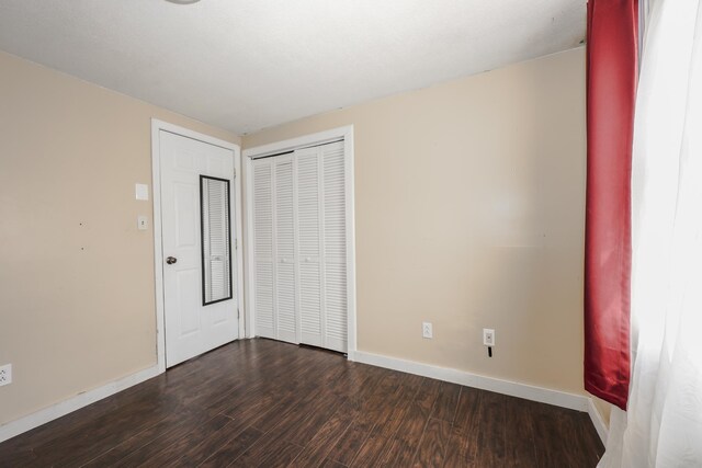 unfurnished bedroom featuring dark wood-style floors, baseboards, and a closet