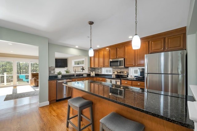 kitchen with light wood finished floors, a breakfast bar, hanging light fixtures, brown cabinetry, and stainless steel appliances