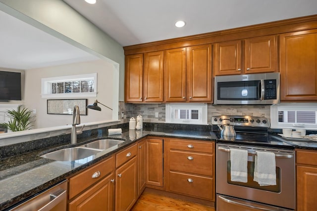 kitchen with a sink, dark stone counters, brown cabinets, and stainless steel appliances