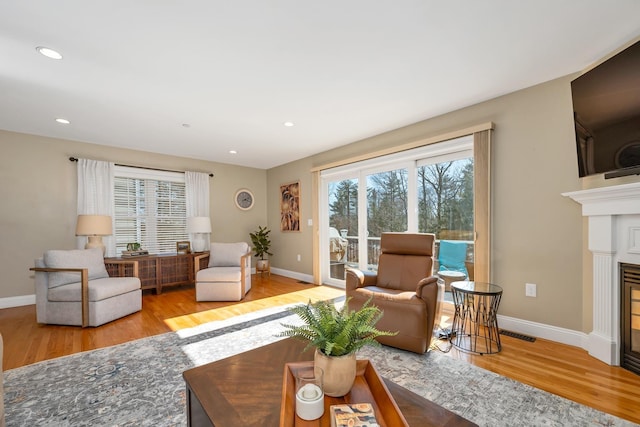 living area featuring visible vents, baseboards, recessed lighting, wood finished floors, and a glass covered fireplace