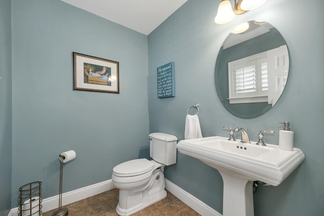 half bathroom featuring tile patterned floors, toilet, baseboards, and a sink