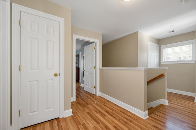 hallway with visible vents, an upstairs landing, light wood-type flooring, and baseboards