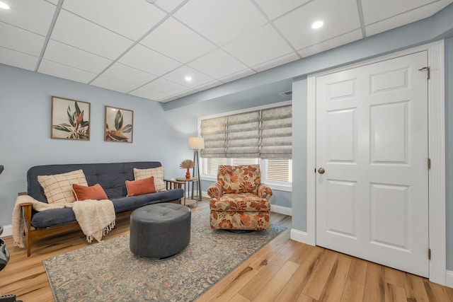 living area featuring a paneled ceiling, baseboards, and wood finished floors