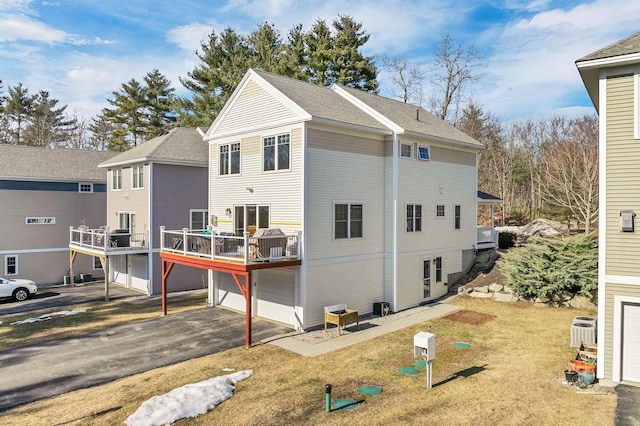 back of house with central air condition unit, a lawn, a garage, a deck, and driveway