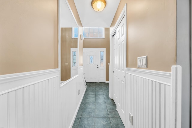 corridor featuring dark tile patterned flooring and wainscoting