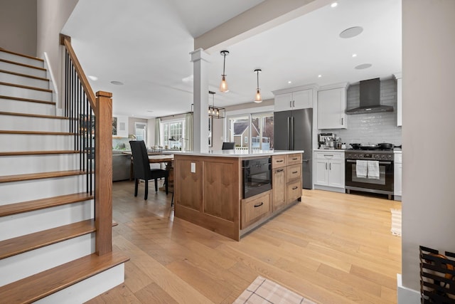 kitchen featuring backsplash, range with gas cooktop, light wood-style floors, high end fridge, and wall chimney exhaust hood