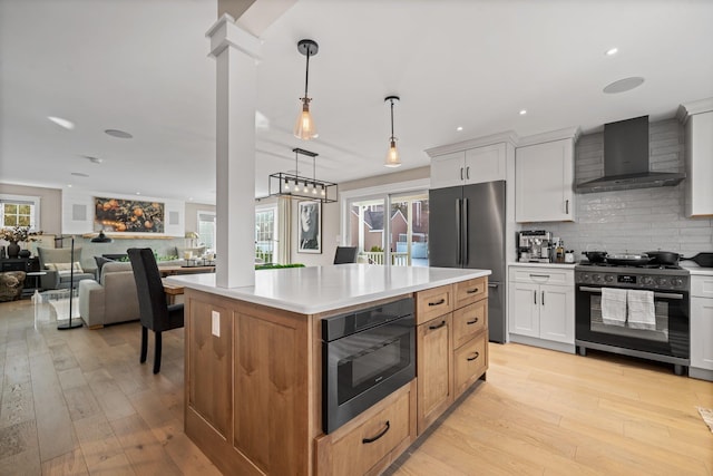 kitchen featuring backsplash, built in microwave, gas range oven, freestanding refrigerator, and wall chimney exhaust hood