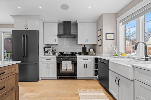 kitchen with freestanding refrigerator, wall chimney exhaust hood, light countertops, black range with gas stovetop, and dishwasher