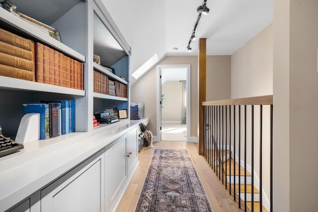 hallway featuring light wood-style floors, rail lighting, and vaulted ceiling