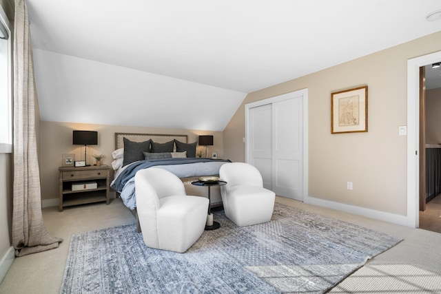 bedroom featuring a closet, light colored carpet, baseboards, and lofted ceiling