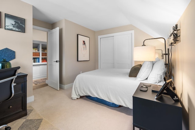 bedroom featuring a closet, baseboards, light colored carpet, and lofted ceiling